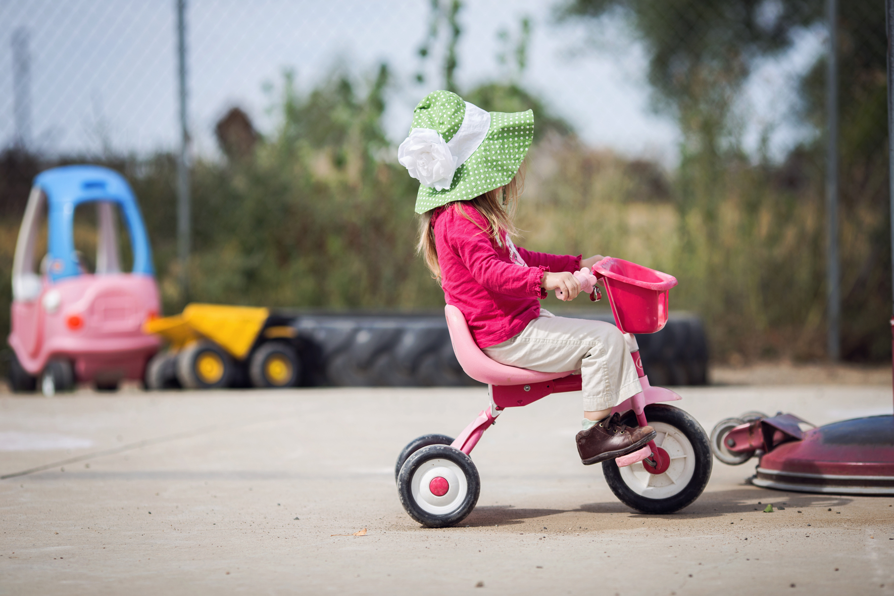 A little girl in a sun hat riding a tricycle on the Highway 312 daycare playground
